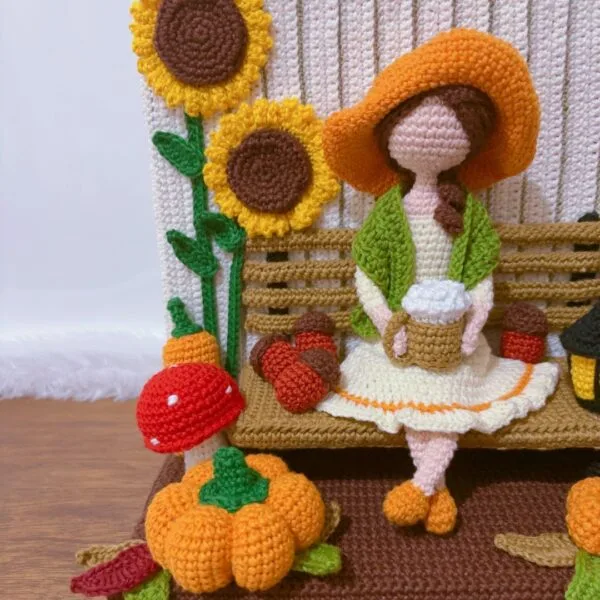 crochet Fall or Autumn decoration with a girl sitting on a bench drinking coffee, surrounded by pumpkins, mushroom, spider, barrel, sunflower