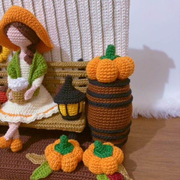 crochet Fall or Autumn decoration with a girl sitting on a bench drinking coffee, surrounded by pumpkins, mushroom, spider, barrel, sunflower