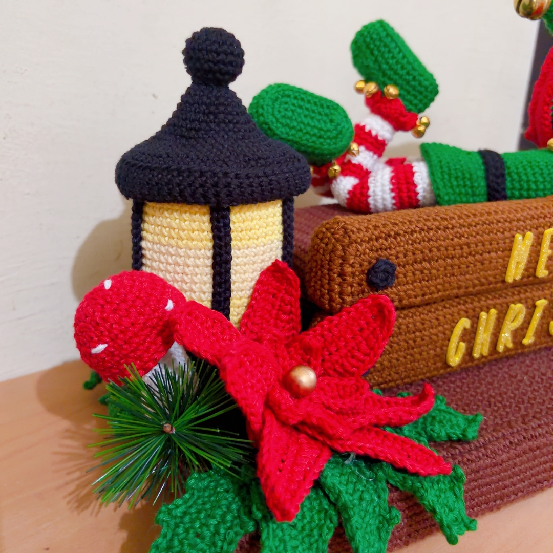 crochet elf on crochet wood, surrounded by poinsettias, holly leaves, mushrooms and a lantern